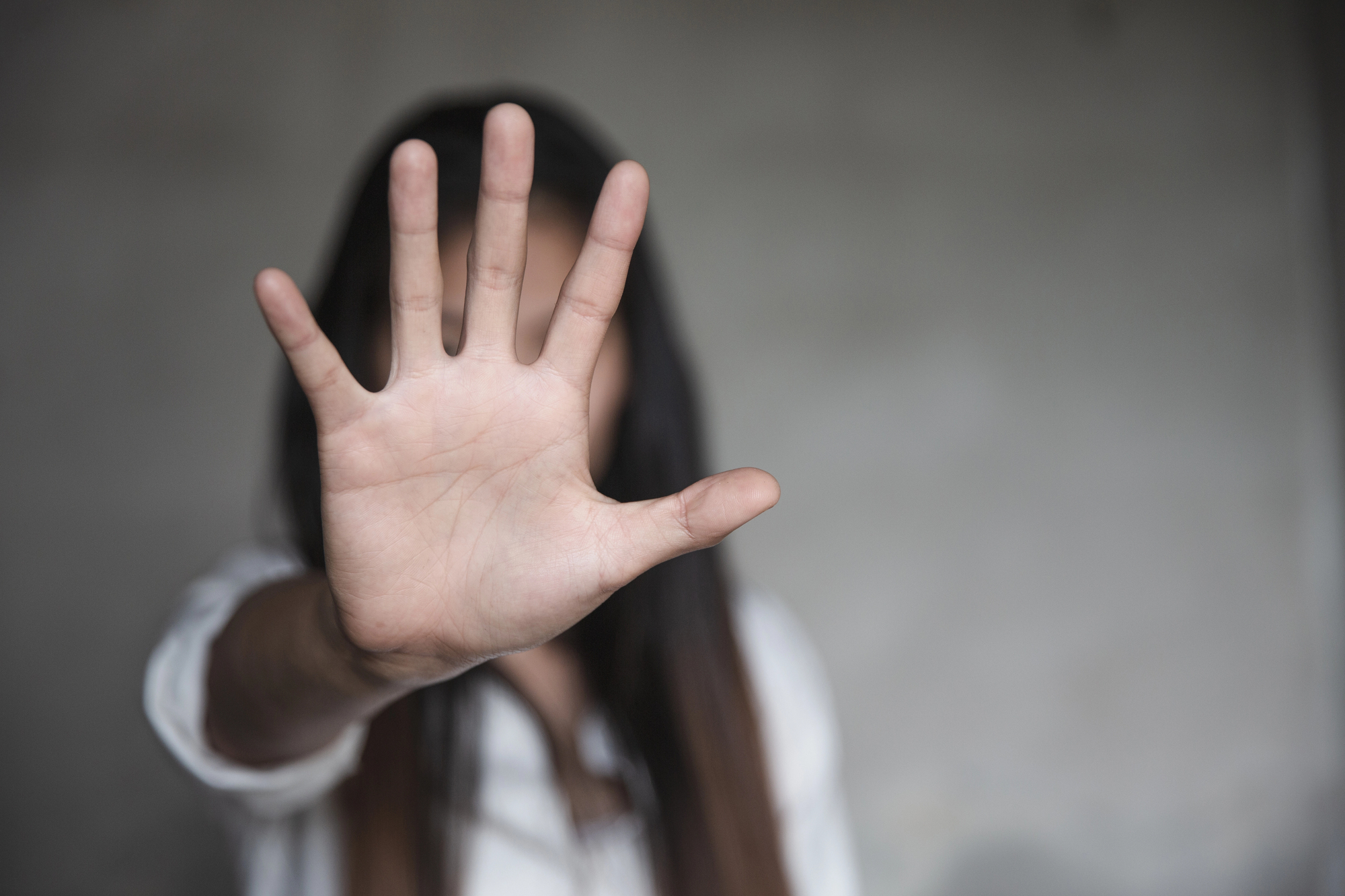Mulher com a mão erguida à frente do rosto, dissuadindo investidas contra ela.