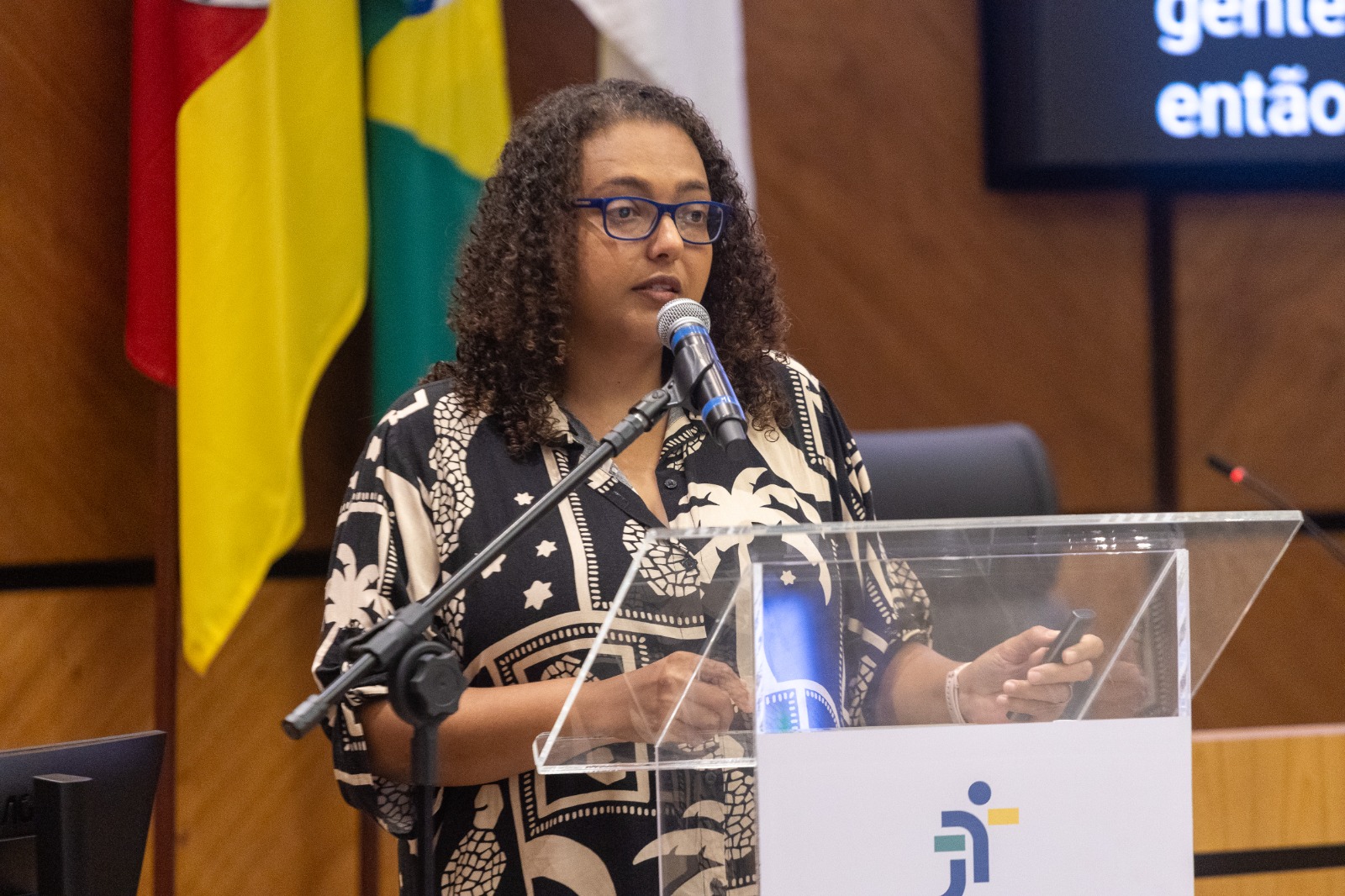 Bábara é negra, tem cabelos crespos e usa óculos de aro grande. lusa blusa estampada e fala no púlpiito