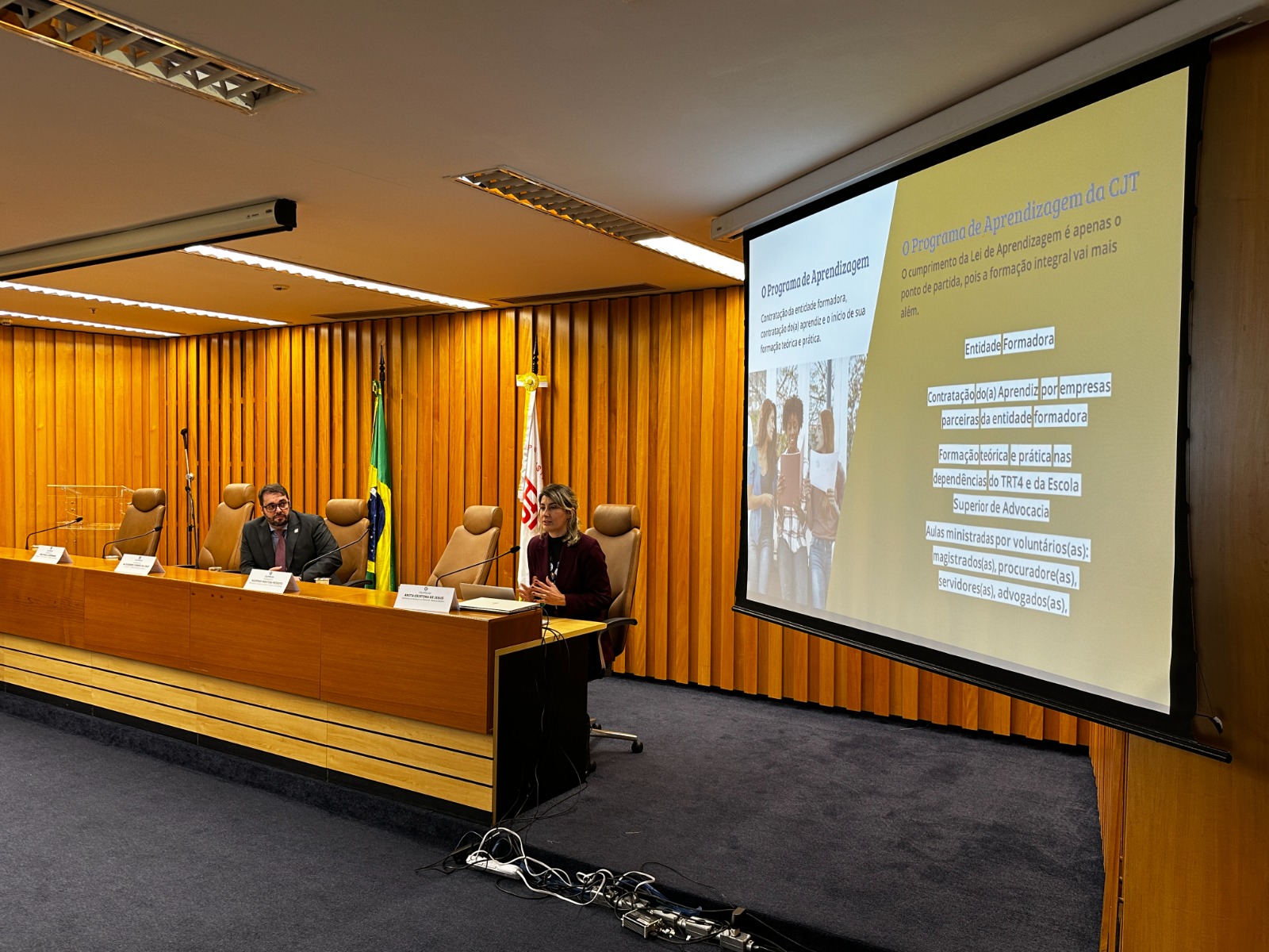 A foto mostra o des. alexandre falando e anita ao lado numa mesa.