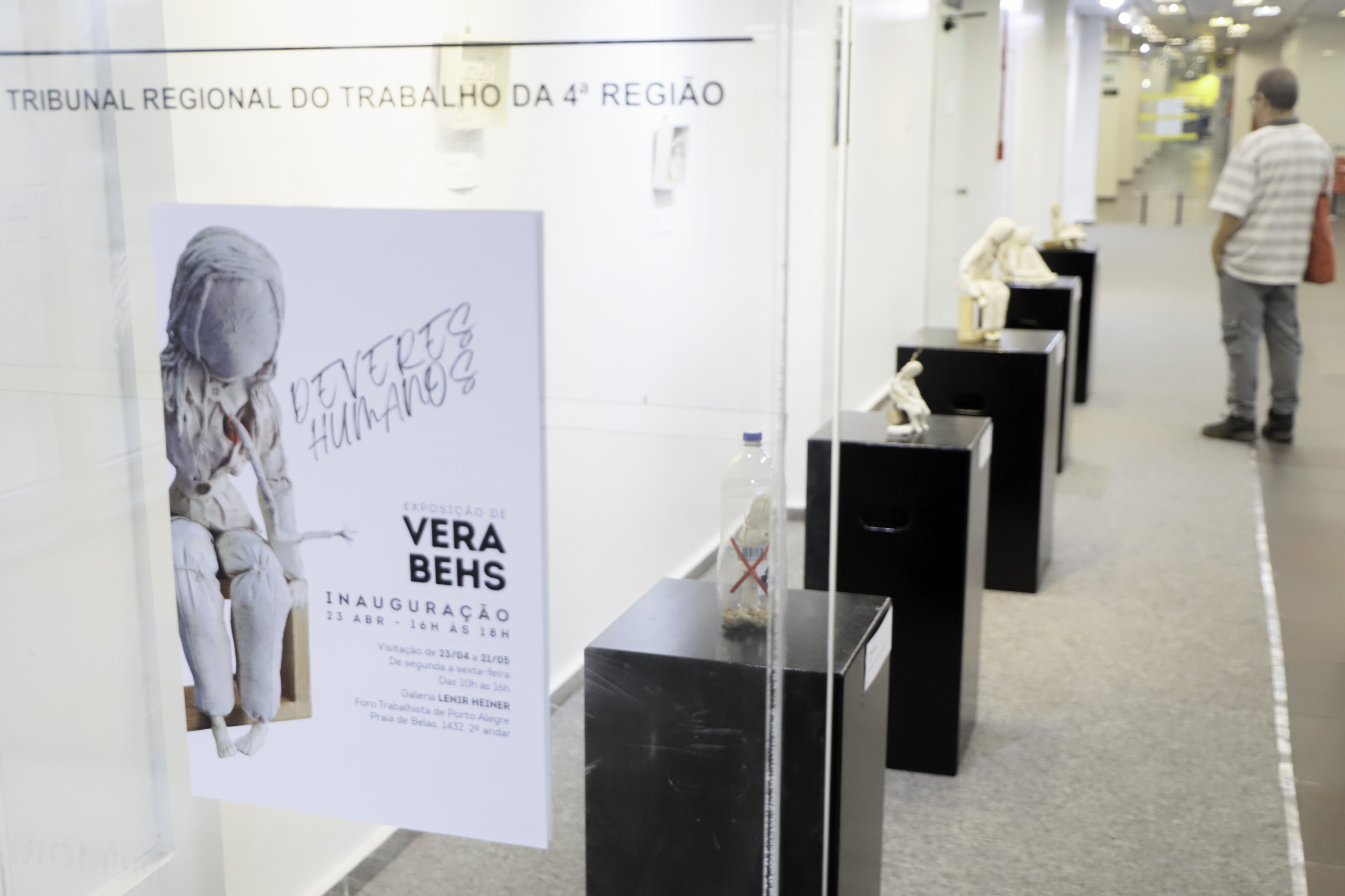 Cartaz da exposição com as obras ao fundo e um visitante observando.