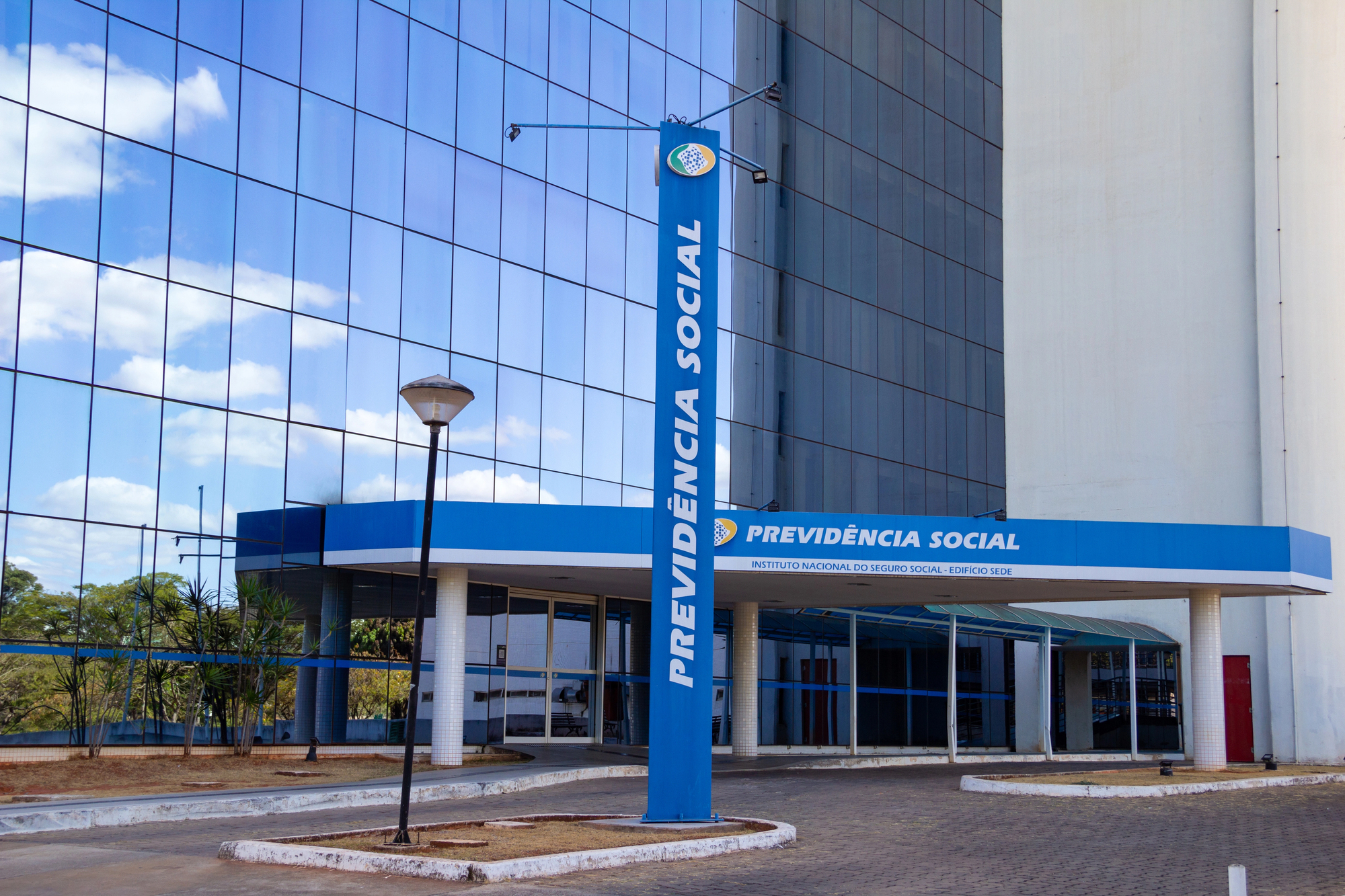 A imagem mostra a fachada da sede do INSS em Brasília. Trata-se de um prédio espelhado e em tons de azul.
