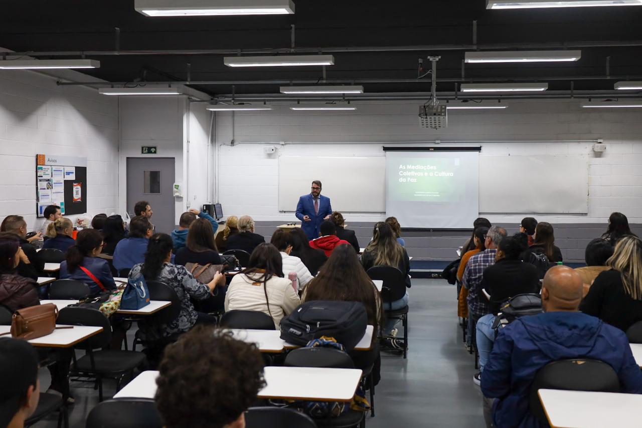 Foto do presidente Alexandre Cruz palestrando para os alunos, em uma sala de aula. Magistrado está em pé, e os alunos, sentados.