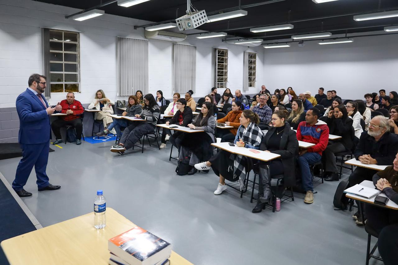 Foto do presidente Alexandre Cruz palestrando para os alunos, em uma sala de aula. Magistrado está em pé, e os alunos, sentados.