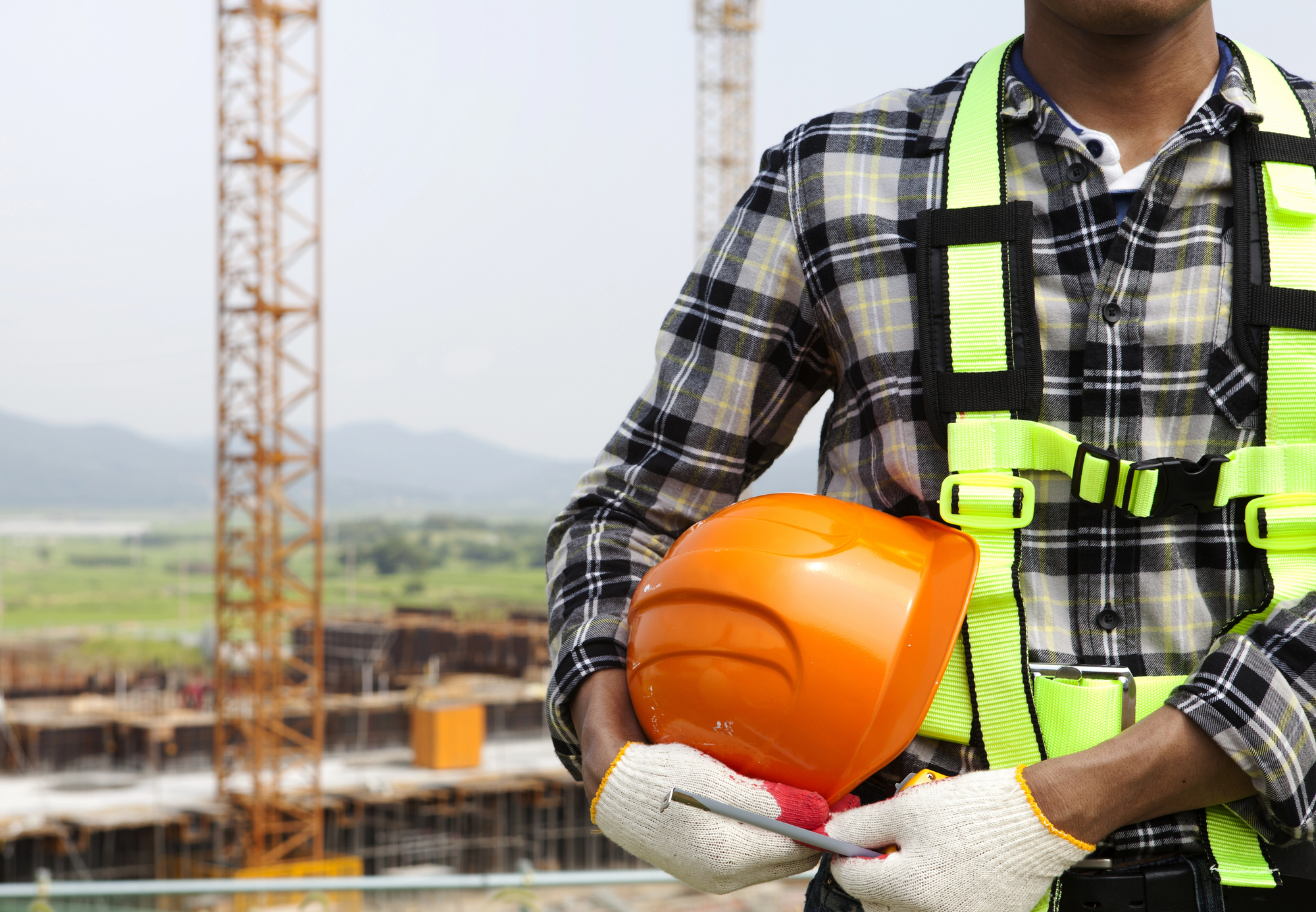 Close em trabalhador de construção segurando um capacete de segurança e usando luvas de proteção.