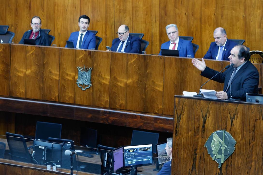 Foto da sessão. Um parlamentar discursa no púlpito. Ao fundo, a mesa de autoridades.