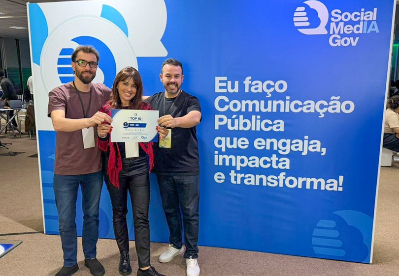 Daniel Aguiar, Camila Dotto e Eduardo Matos, com o certificado na mão, em frente ao banner do evento.