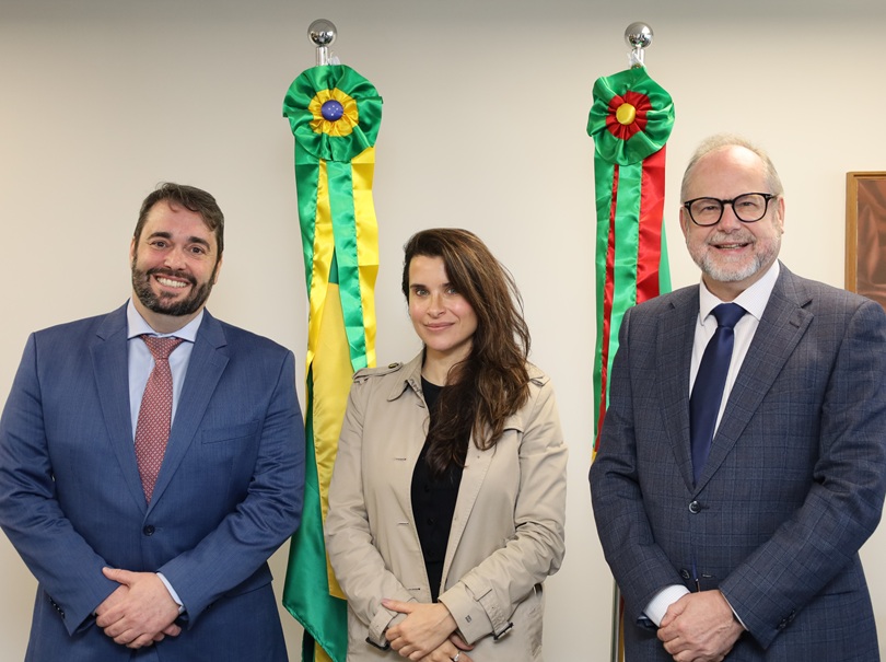A fotografia mostra, em pé, lado a lado, o presidente do TRT-RS, desembargador Alexandre Corrêa da Cruz, a juíza Carolina Paiva, e o 1º  vice-presidente do Tribunal de Justiça do Estado do Rio Grande do Sul (TJ-RS), desembargador Cláudio Luís Martinewski.