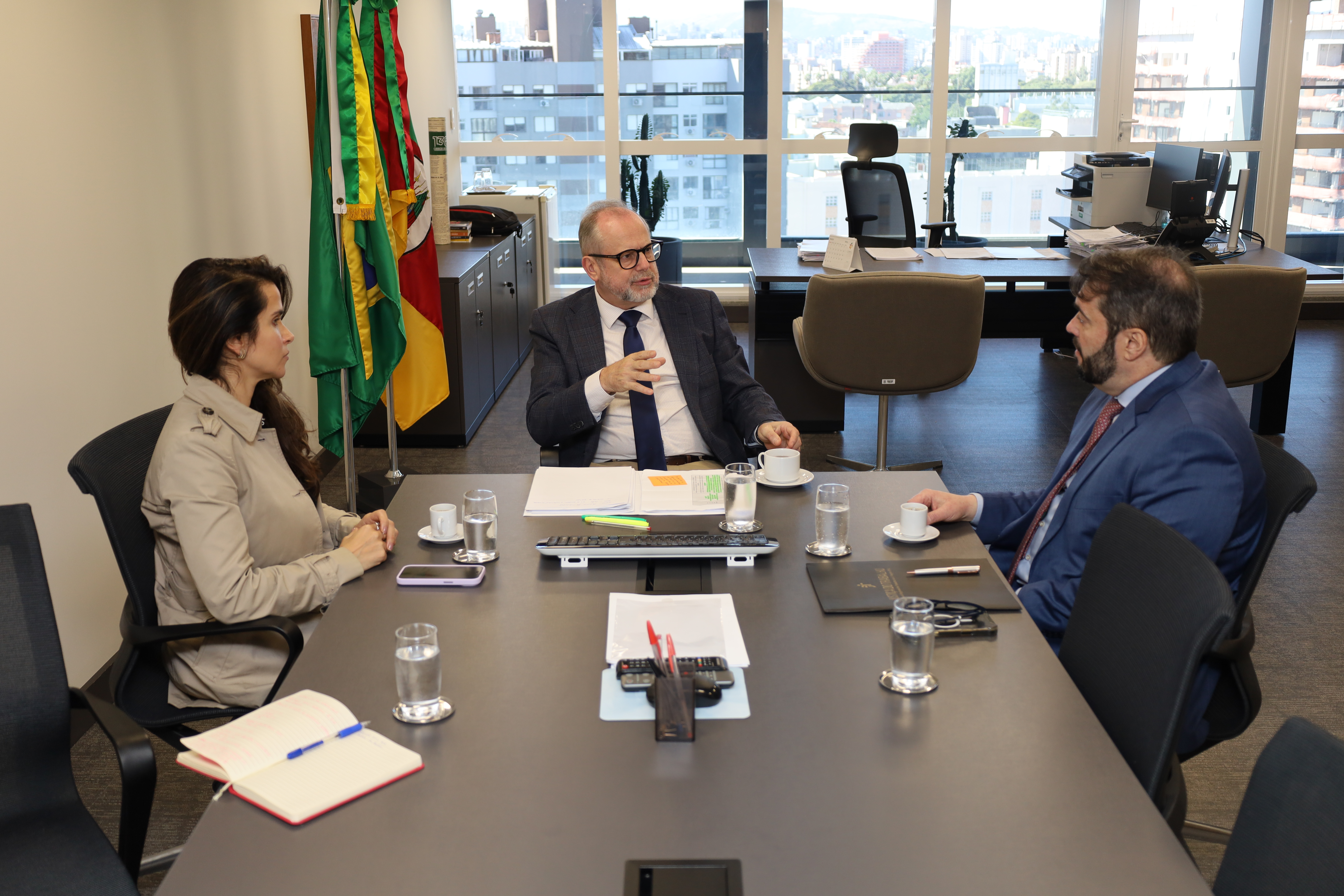 A fotografia mostra, sentados à mesa de reuniões, conversando, da esquerda para a direita, a juíza Carolina Paiva, o desembargador Cláudio Luís Martinewski e o presidente do TRT-RS, desembargador Alexandre Corrêa da Cruz.