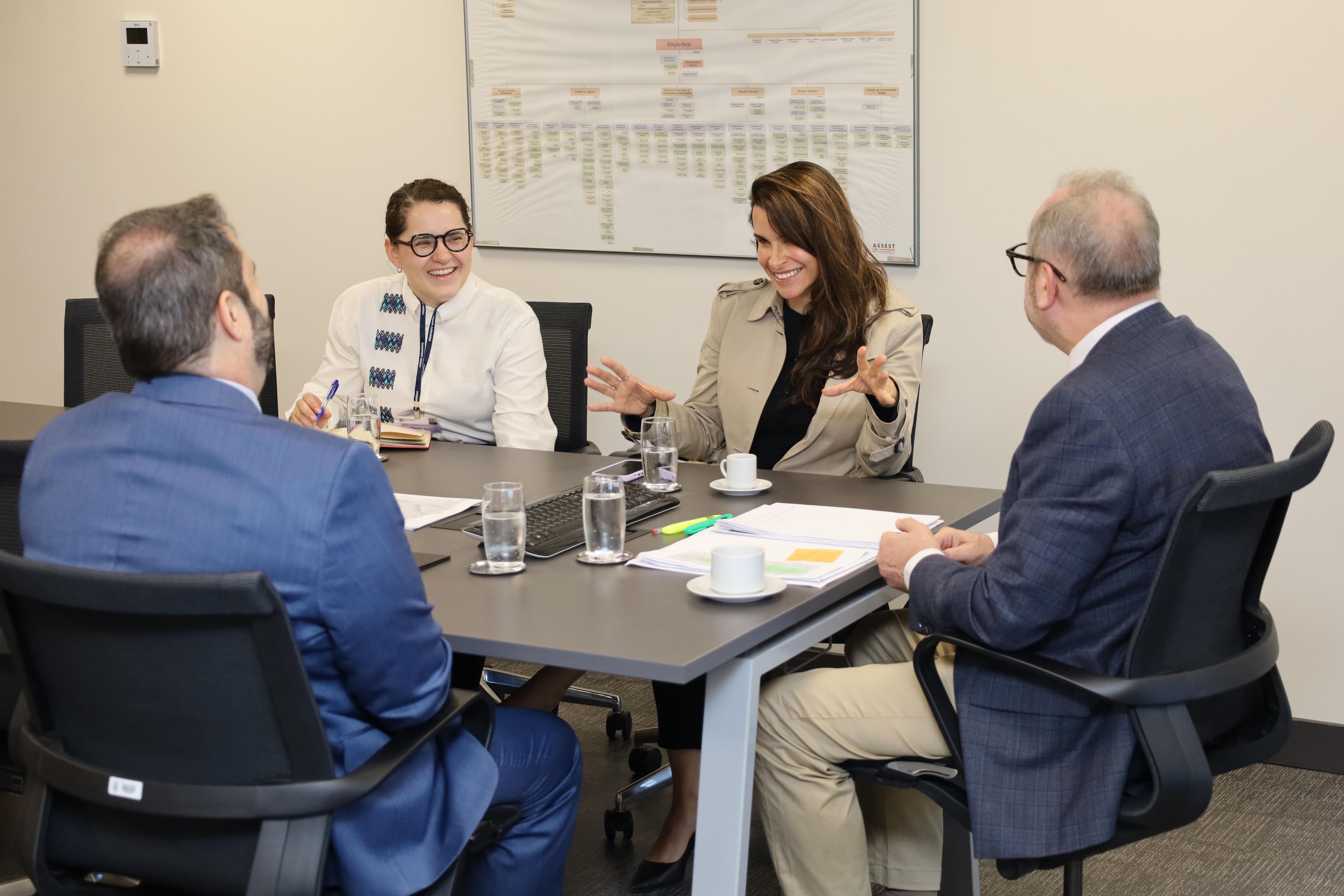A fotografia mostra, sentados à mesa de reuniões, conversando, da esquerda para a direita, a secretária de Desembargador e pesquisadora, Marina de Almeida Rosa, de frente para o fotógrafo, a juíza Carolina Paiva,  também de frente para o fotógrafo, o desembargador Cláudio Luís Martinewski de lado para o fotógrafo, e o presidente do TRT-RS, desembargador Alexandre Corrêa da Cruz.