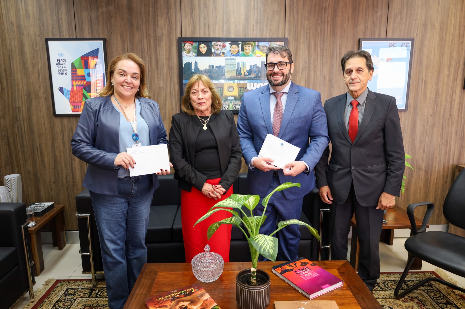 A foto mostra quatro pessoas posando para foto, duas delas com convites em mãos.