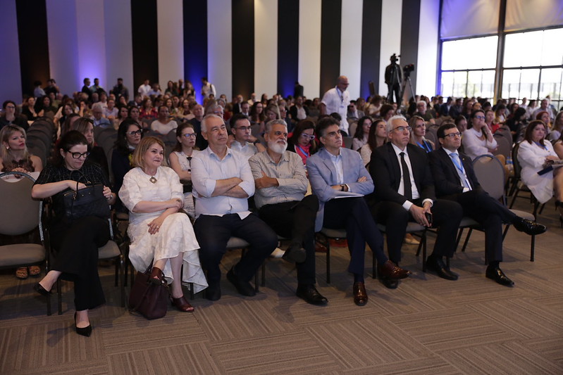 Foto em primeiro plano do presidente palestrando, com demais painelistas ao lado, na mesa do painel.