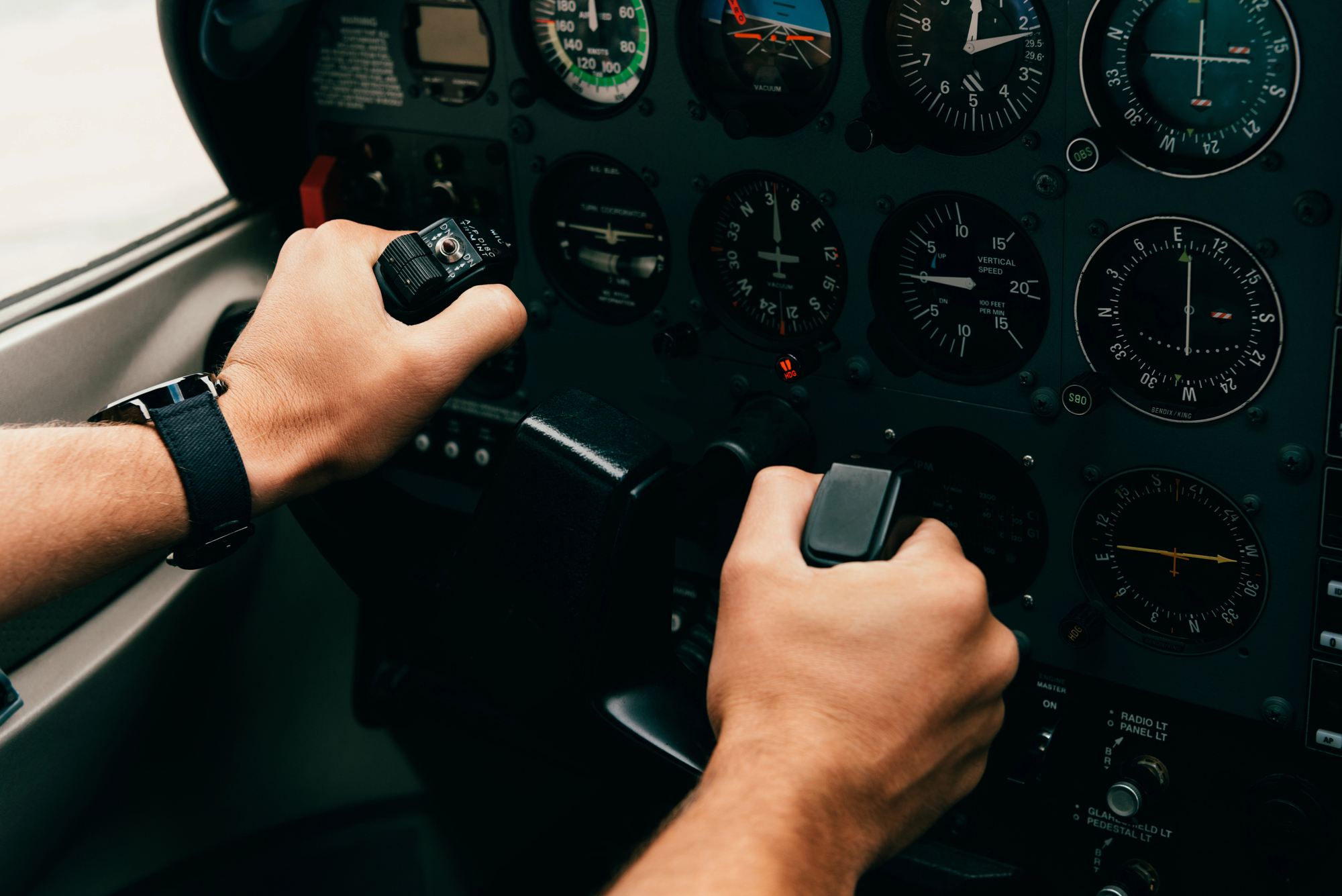 Visão parcial das mãos de um piloto de avião segurando o manche da aeronave.