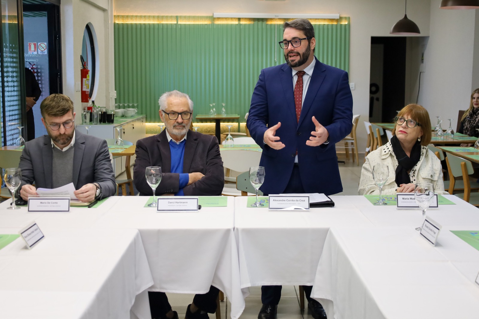 A foto mostra des. Alexandre ao lado três pessoas numa mesa.