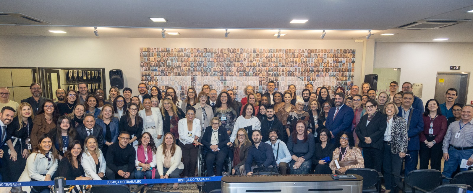 A foto mostra diversas pessoas posando para foto em frente ao Painel de Pessoas do TRT-RS.