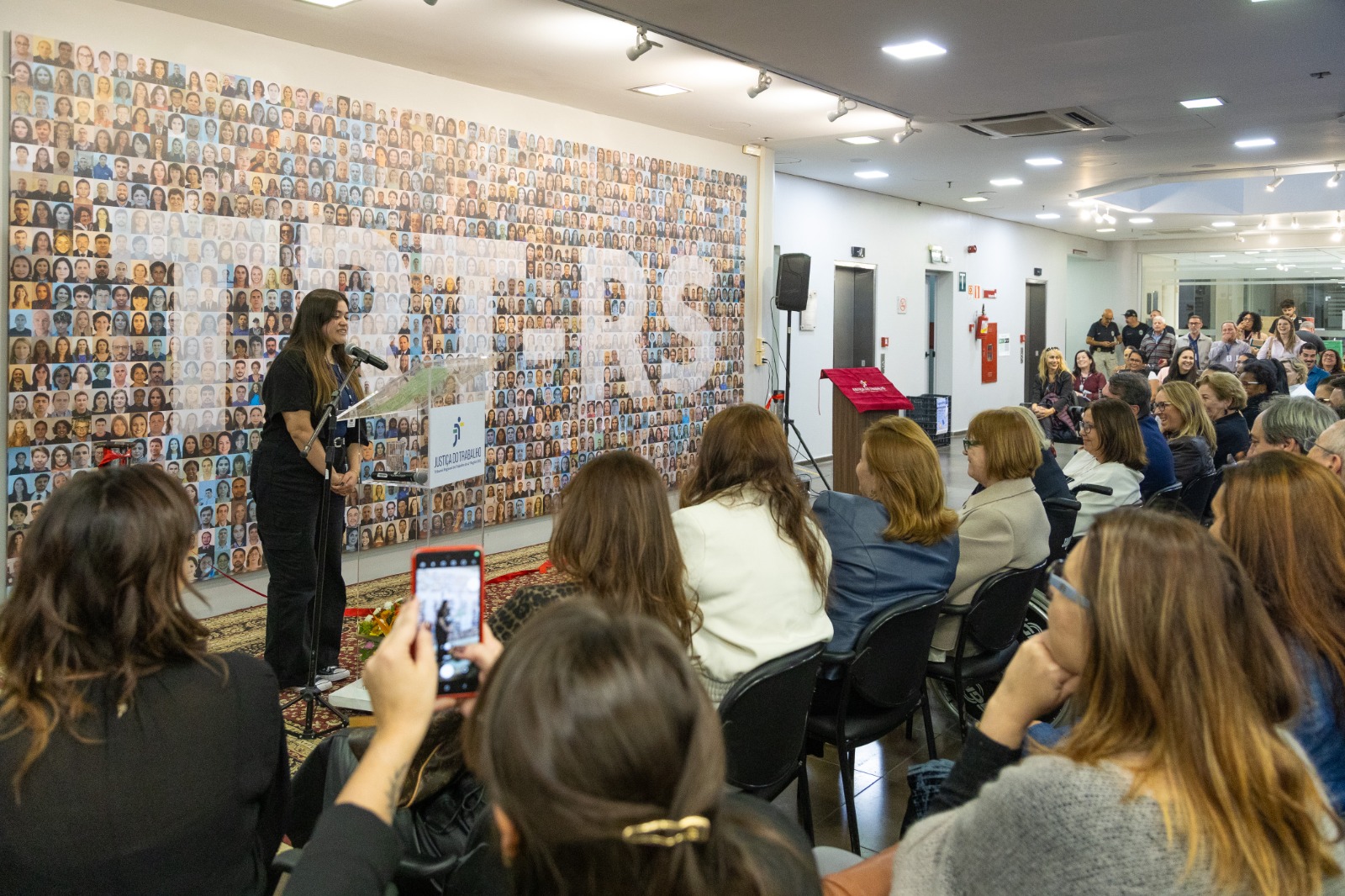 A foto mostra a estagiária Priscila discursando em frente ao público.