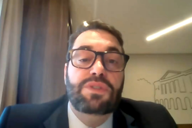 Presidente do TRT-RS, desembargador Alexandre Corrêa da Cruz, é um homem de meia idade, com a pele clara e cabelos e barba castanho escuro. Ele usa um terno preto. Ao fundo, há uma parede com a pintura do que parece ser um prédio antigo, na cor bege.