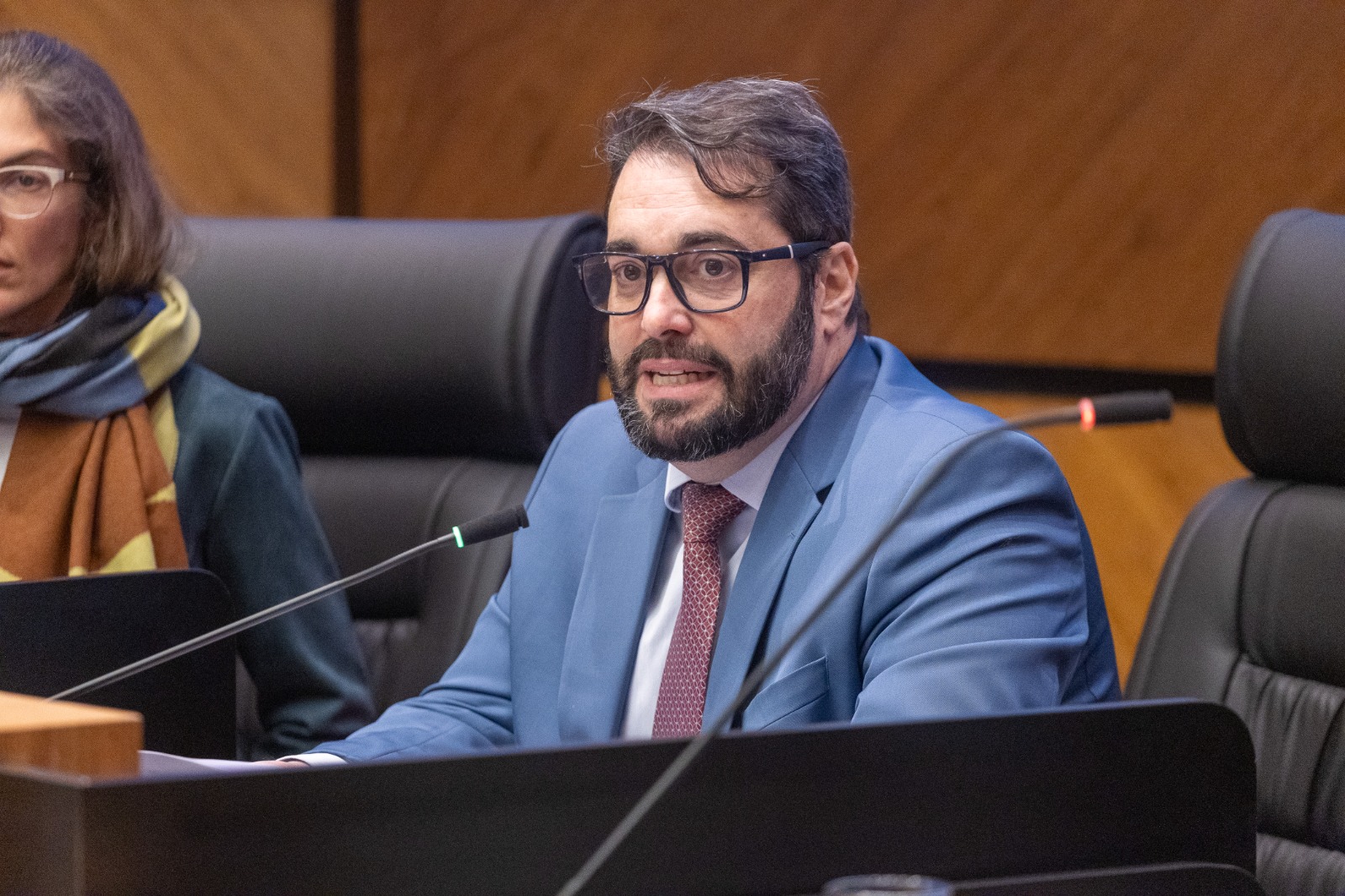 Alexandre é branco, usa barba e cabelo pretos. veste terno azul e fala na mesa oficial. 