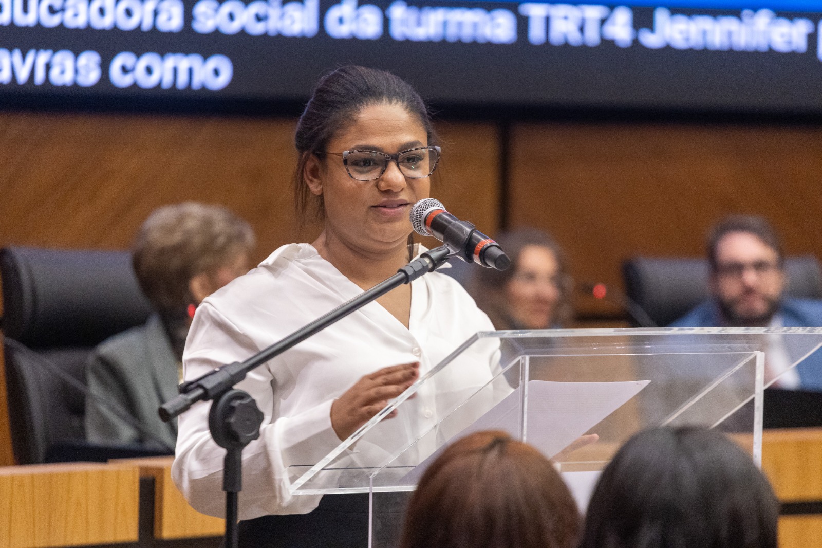 Dienifer é negra e usa cabelo curto. veste blusa branca e fala no púlpito. 