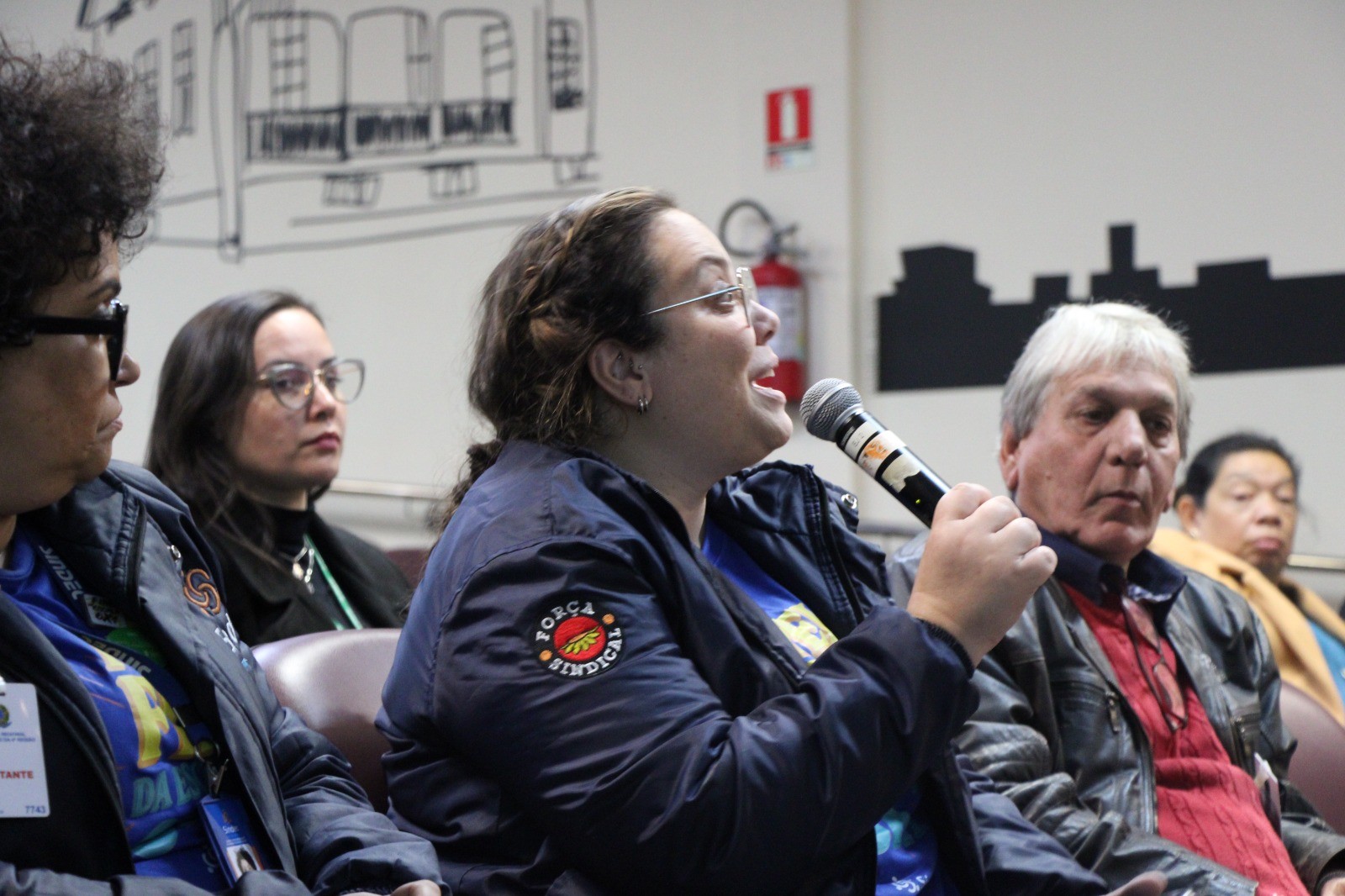 Representante de associação sindical falando ao microfone, durante a audiência pública