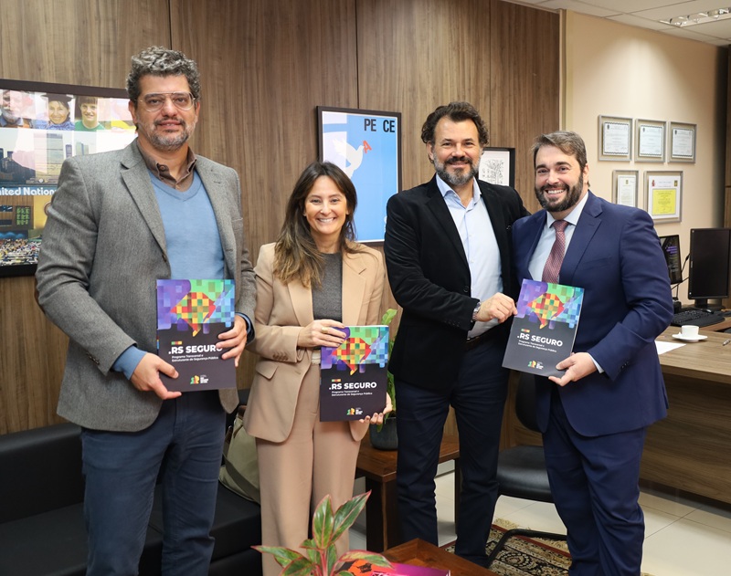 A fotografia mostra os presentes na reunião, em pé, lado a lado, no gabinete da Presidência, sorrindo, sendo que os representantes do TRT seguram as cópias da cartilha em mãos.