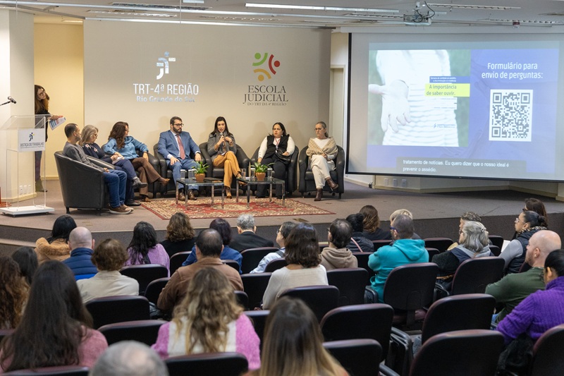 A fotografia mostra a plateia do auditório sentada, de costas, e voltados para a foto estão os participantes da roda de conversa.
