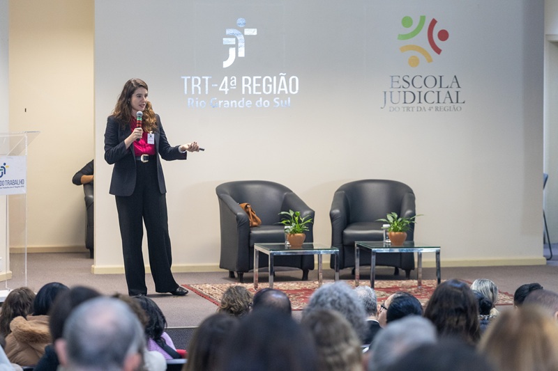 A fotografia mostra a procuradora do trabalho, Larissa Menine Alfaro, palestrando sobre o palco