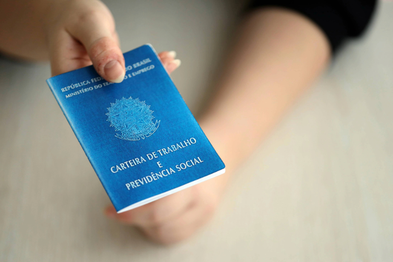 Mulher segurando Carteira de Trabalho. Ela tem a pele branca. O rosto não é mostrado.