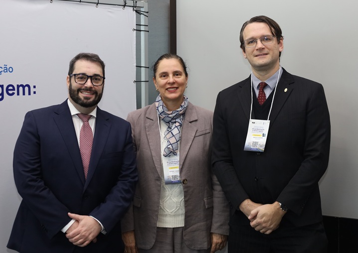 A fotografia mostra o presidente Alexandre, a desembargadora Luciane e o juiz Fabrício posando, lado a lado, em frente ao painel de divulgação do evento.