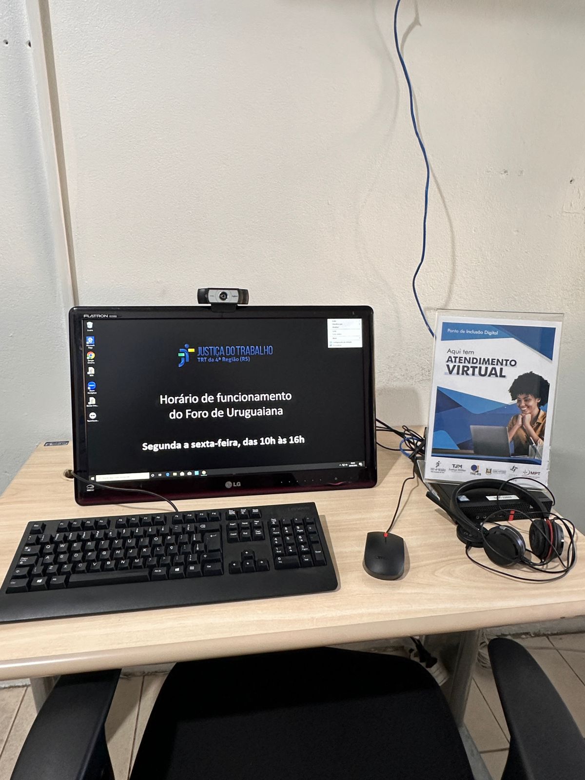 A imagem mostra um Ponto de Inclusão Digital sobre uma mesa clara. Há um monitor com tela preta informando: "JUSTIÇA DO TRABALHO TRT da 4ª Região (RS) / Horário de funcionamento do Foro de Uruguaiana / Segunda a sexta-feira, das 10h às 16h". Uma webcam está no topo.