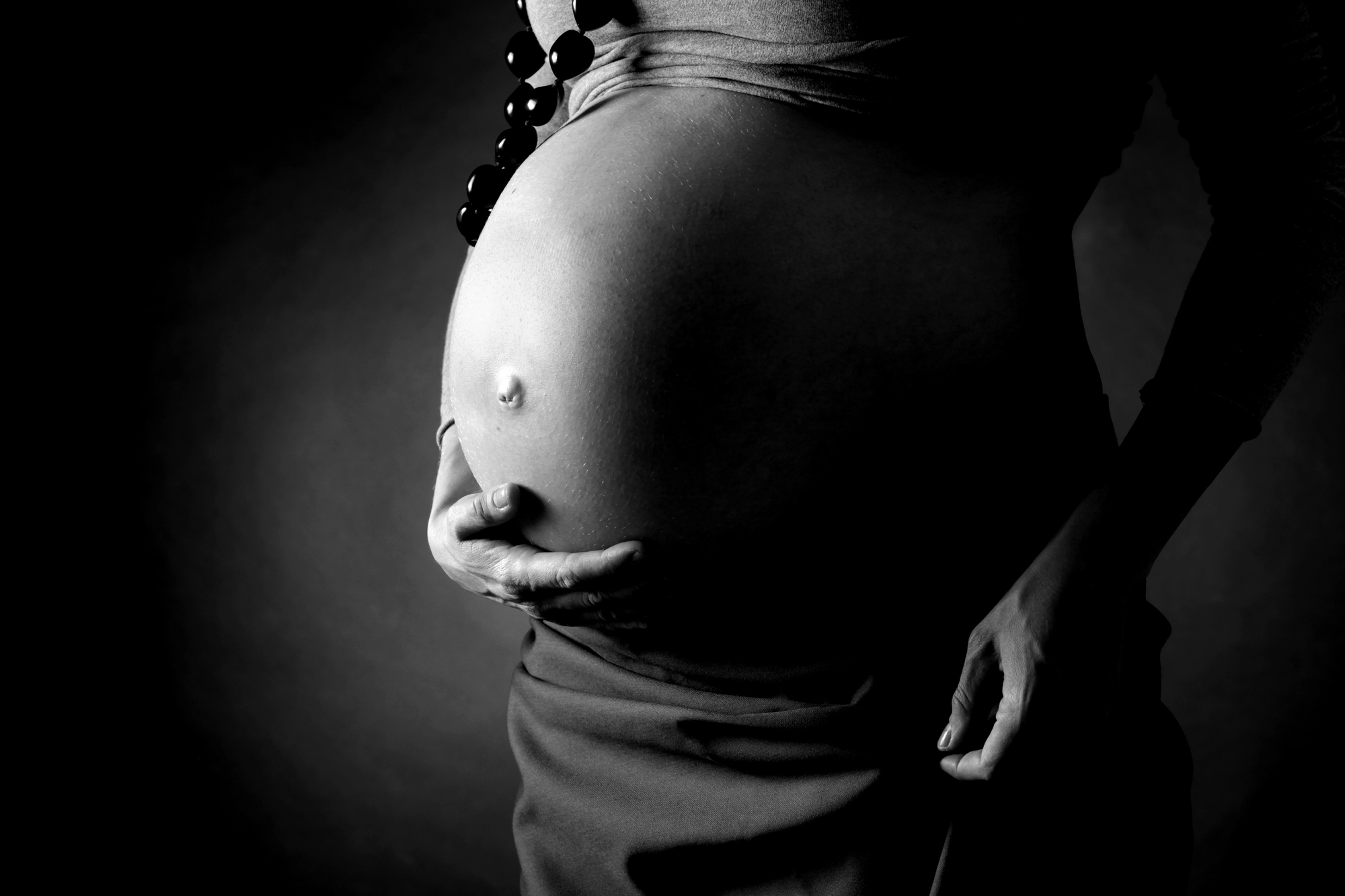 A fotografia é um close, em preto e branco, do ventre de uma gestante.