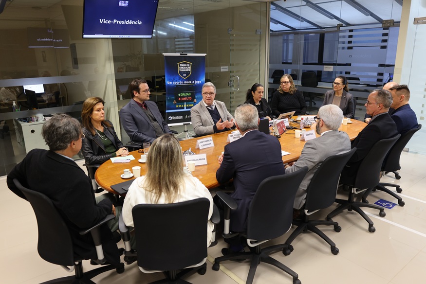 Foto da audiência, com os participantes sentados à mesa de reuniões no Cejusc 2º Grau