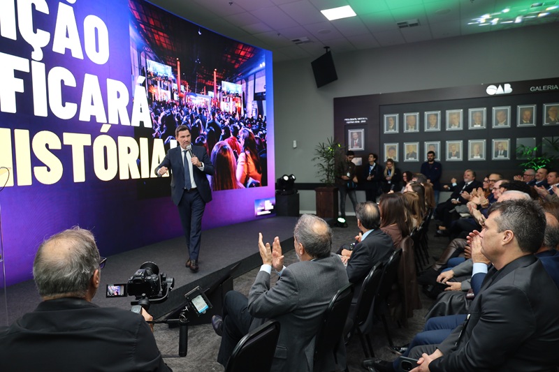 A fotografia mostra o presidente da OAB/RS, Leonardo Lamachia, em seu discurso, no palco. Atrás dele, há um telão com a apresentação do evento