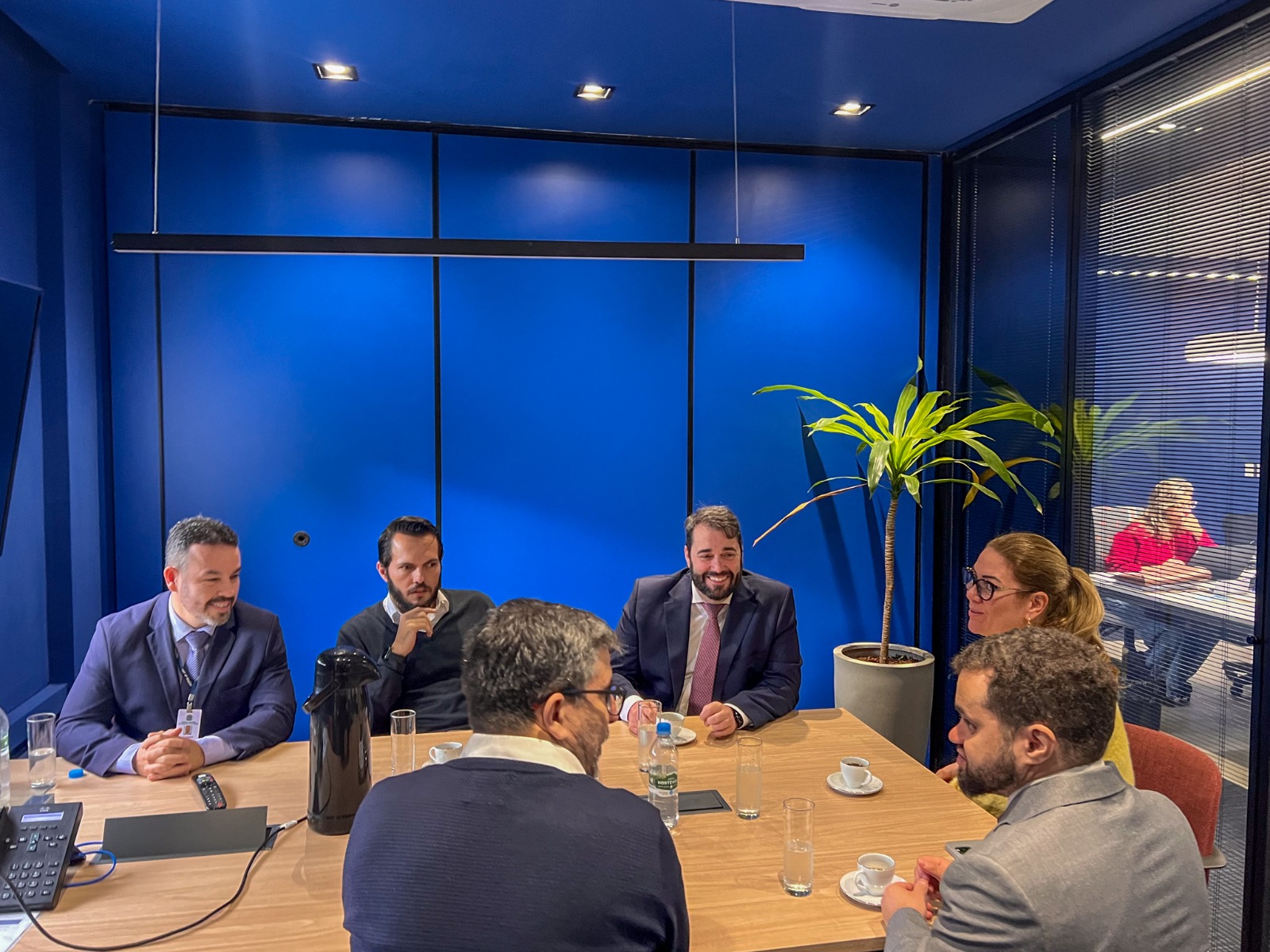 A foto mostra seis pessoas sentadas ao redor de uma mesa em reunião