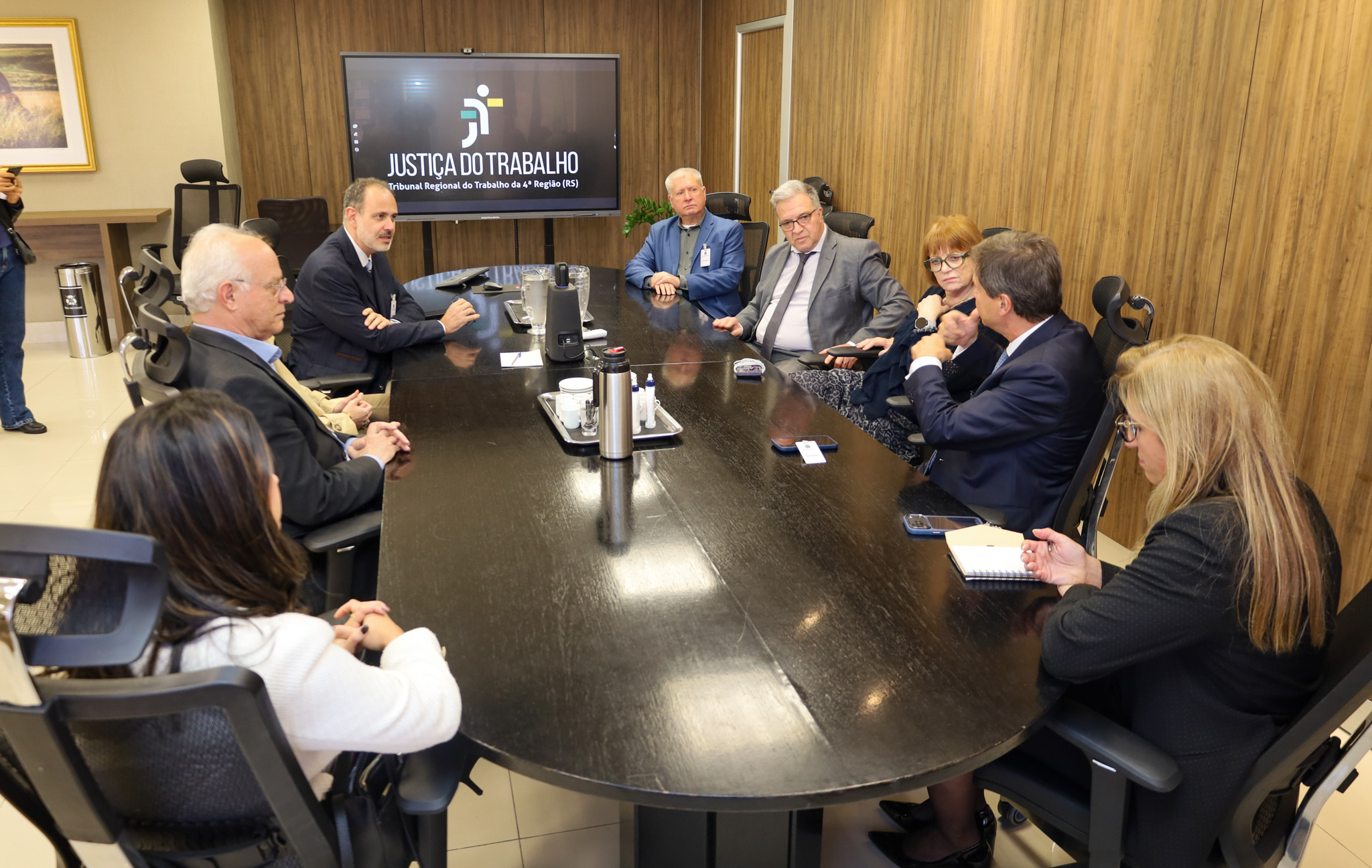 A foto mostra pessoas sentadas ao redor de uma mesa em reunião.