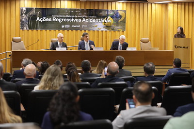 Foto em ângulo aberto do evento, mostrando mesa oficial e público.