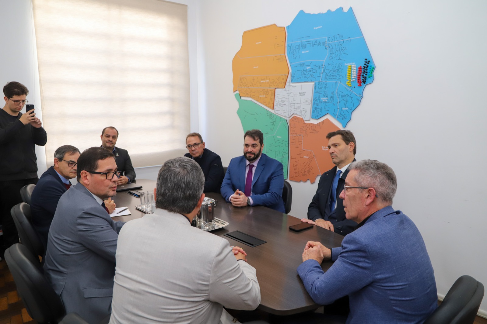 A foto mostra pessoas sentadas reunidas ao redor de uma mesa.