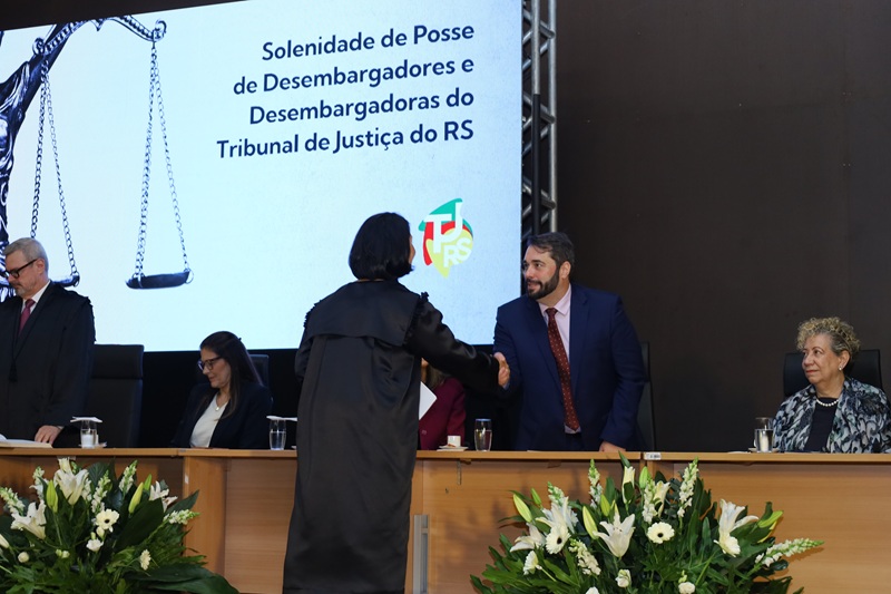 A fotografia mostra o presidente do TRT-RS, na mesa de honra da cerimônia, cumprimentando uma desembargadora recém empossada
