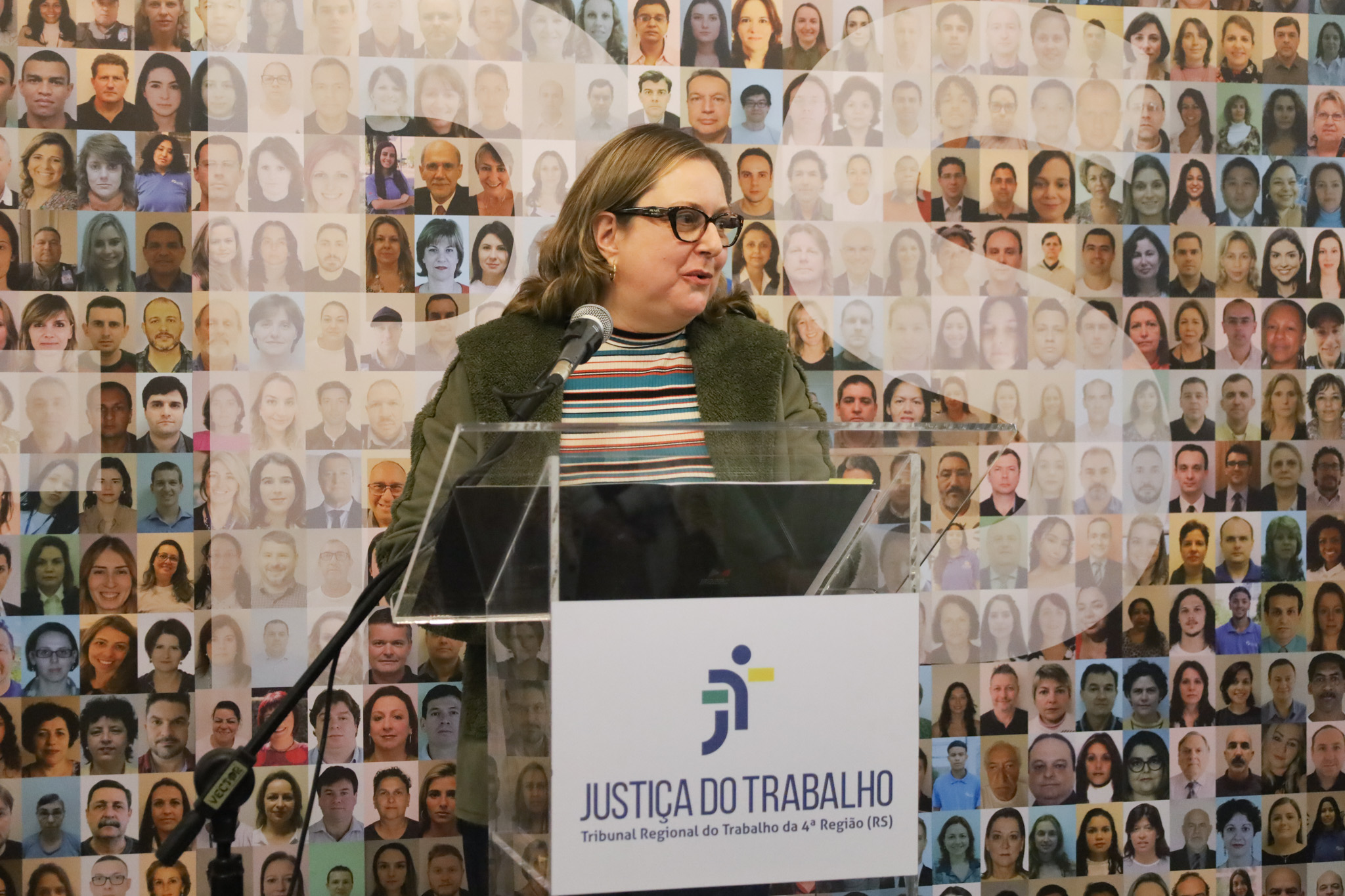 Luciana fala ao microfone atrás de um púlpito de acrílico transparente.