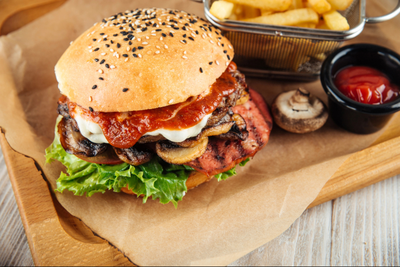 Hambúrguer e batatas fritas, ao lado de um recipiente com molho vermelho e cogumelos.