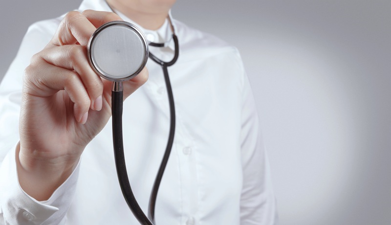 A fotografia mostra, em close, a mão de uma médica segurando um estetoscópio.