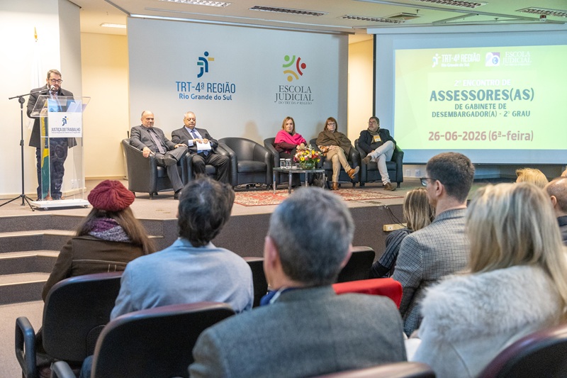 A fotografia mostra o público do evento, de costas, sentado no auditório, enquanto o presidente do TRT discursa no púlpito.