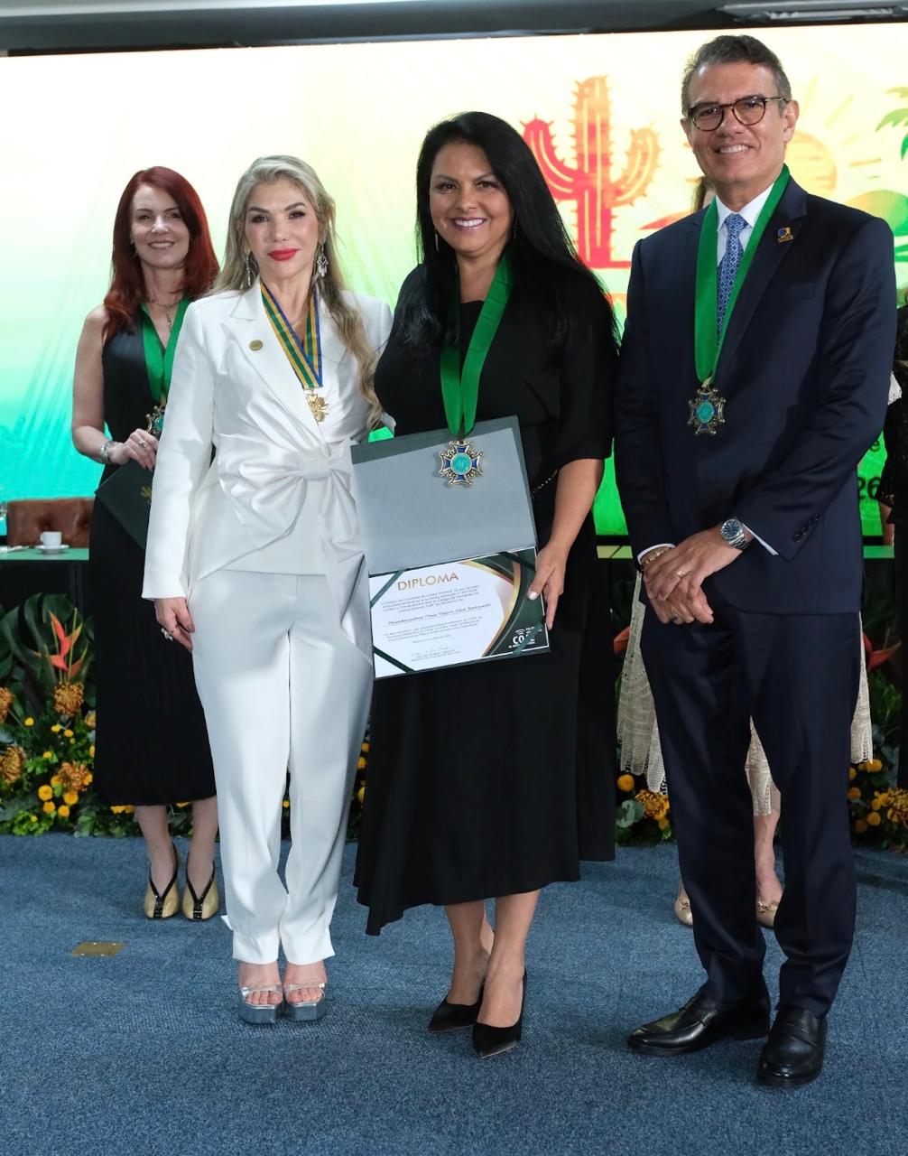 Desembargadora Tânia com medalha e diploma, em foto posada com outras pessoas.