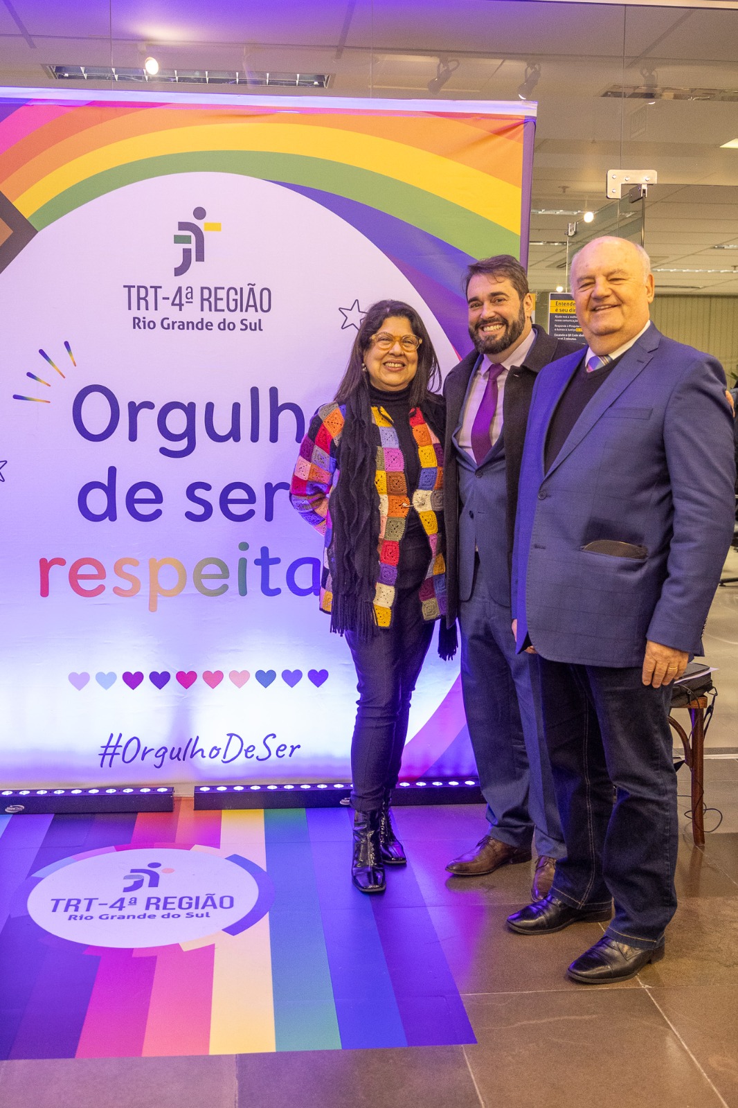 A foto mostra três pessoa posando para foto em frente ao painel da diversidade.