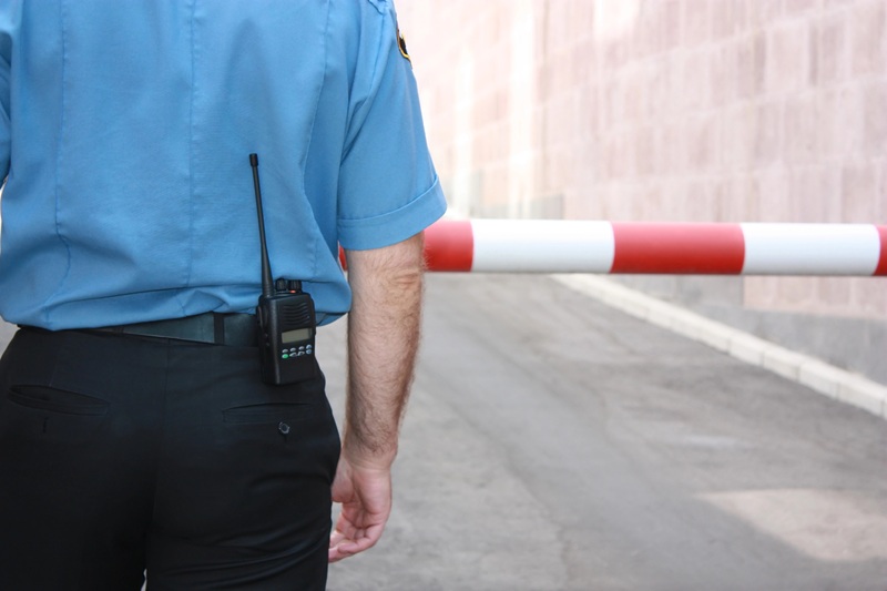A fotografia mostra um vigilante, de costas, sem mostrar o rosto, com um walkie talkie na cintura.