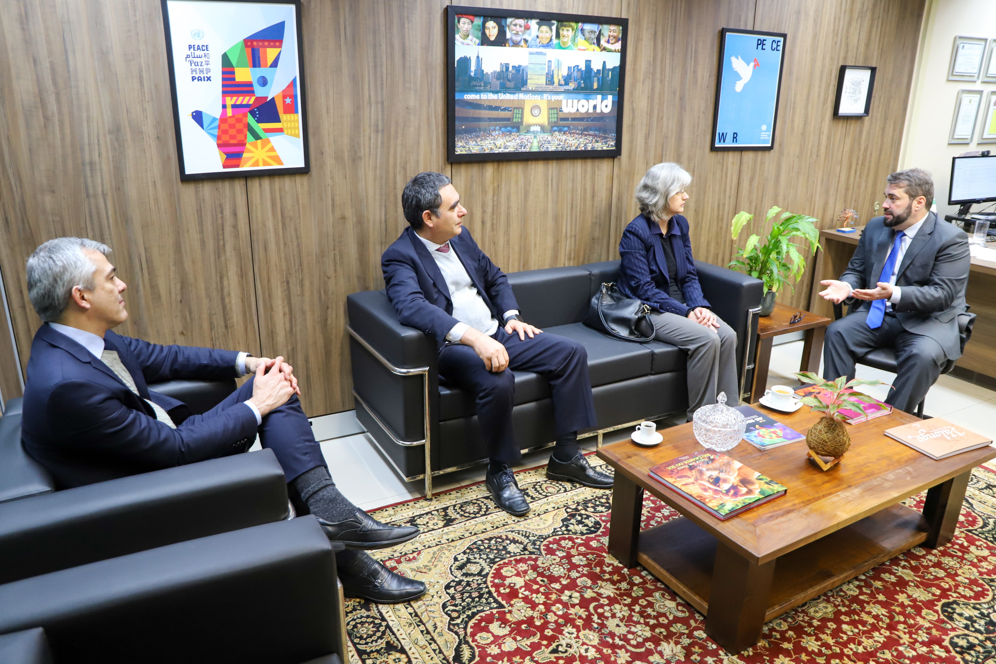 A foto mostra quatro pessoas sentadas em poltronas conversando.