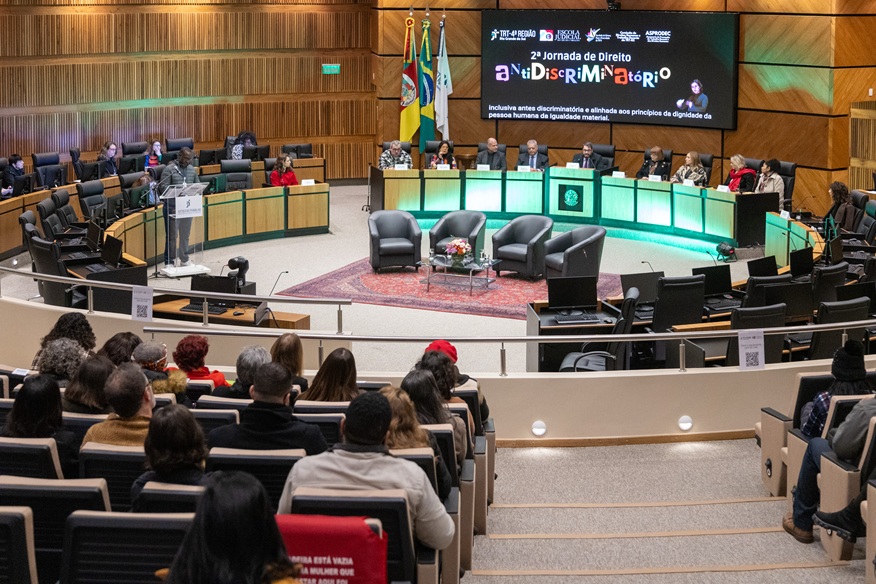 foto em ângulo aberto do plenário, mostrando o público em primeiro plano e, ao fundo, a mesa oficial de abertura e o telão
