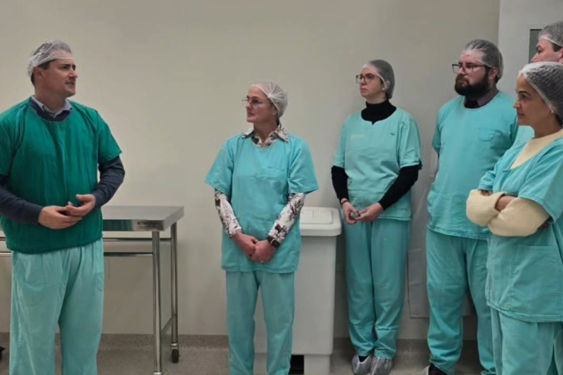 Juíza e integrantes do hospital em área interna da instituição. Eles usam uniforme de bloco cirúrgico, na cor verde água. 