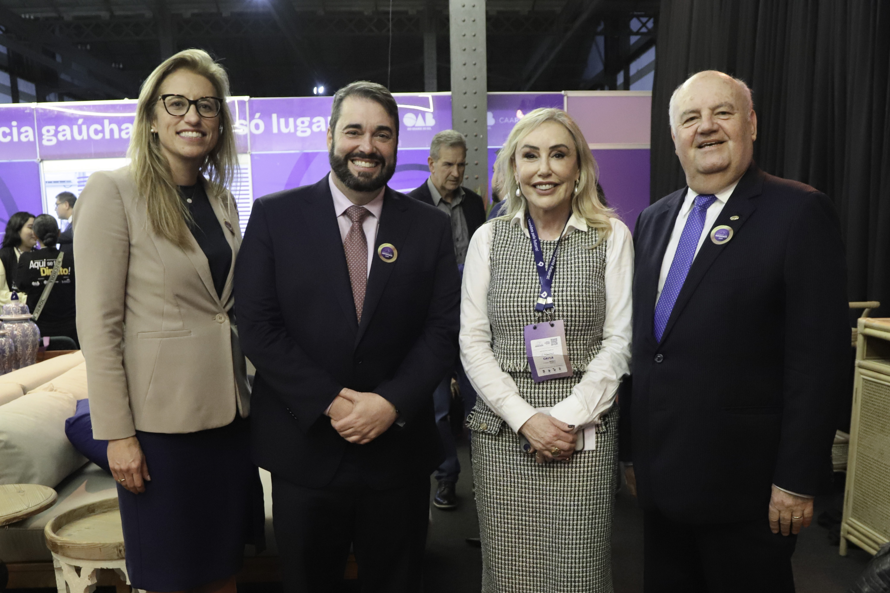 Grupo posa para a foto sorrindo, ao fundo aparece a movimentação de pessoas no evento. 