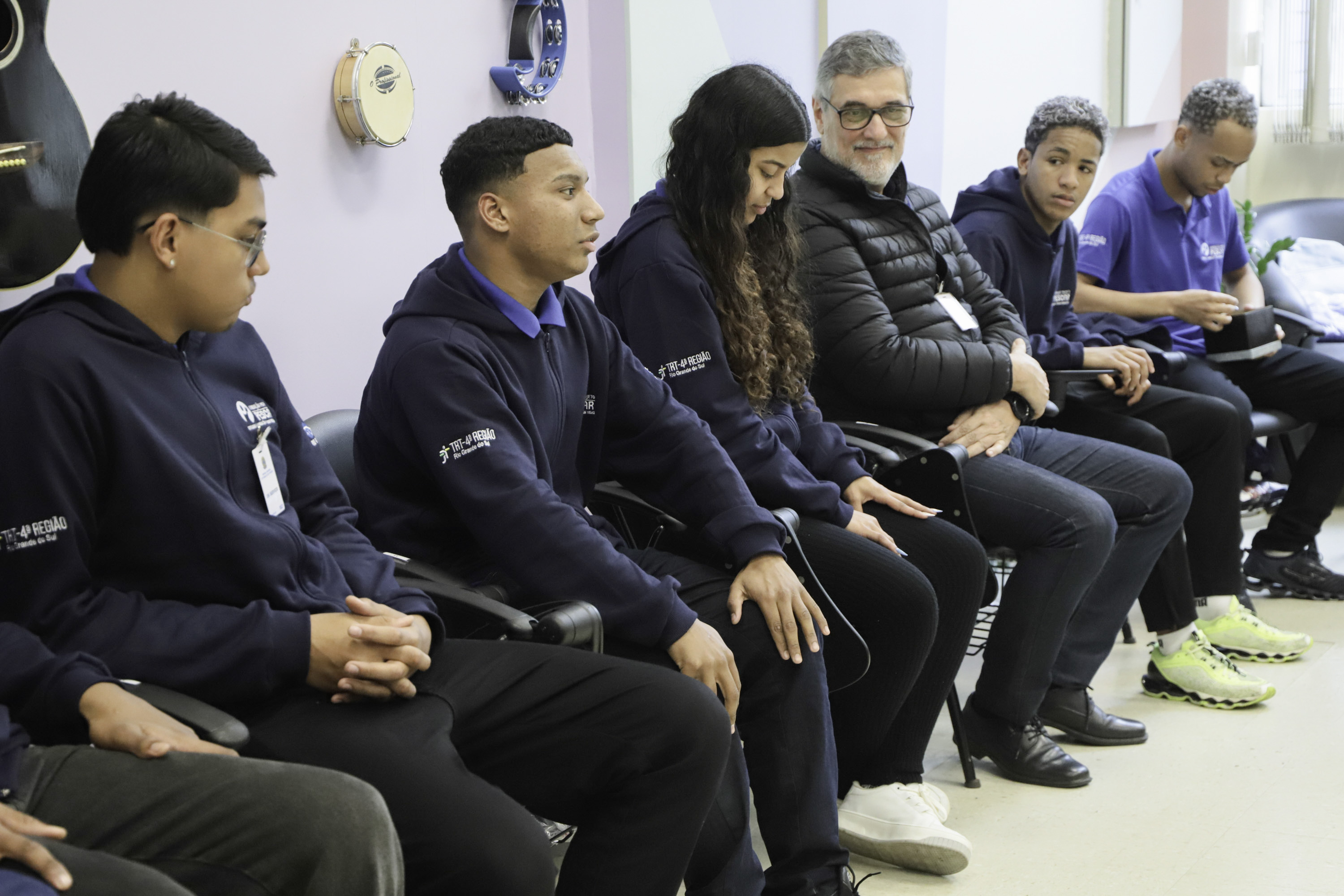 alunos sentados à esquerda. um deles está falando e ao fundo um gestor do TRT observa. 