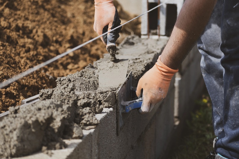 Foto de um pedreiro construindo uma parede, assentando tijolos com cimento.